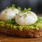 Poached eggs sitting atop avocado toast, garnished with microgreens and black pepper