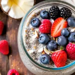 A glass jar of chia seed pudding topped with fresh berries, coconut flakes, and a sprinkle of chia seeds