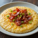 A plate of cheese grits served with crispy bacon and a sprinkle of green onions