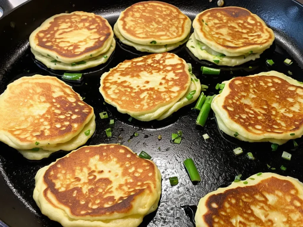 Scallion pancakes frying in a hot skillet, sizzling as they cook