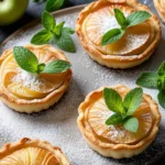 Mini puff pastry apple tarts garnished with powdered sugar and a sprig of mint